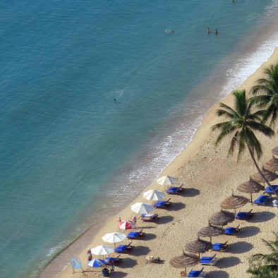 Clean beach with bamboo thatched umbrella and lounge chairs facing sea in Nha Trang